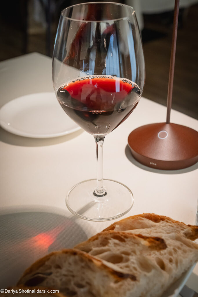 Бокал красного вина и пористый теплый хлеб - начало обеда в ресторане Osteria Al GiGianca в Бергамо